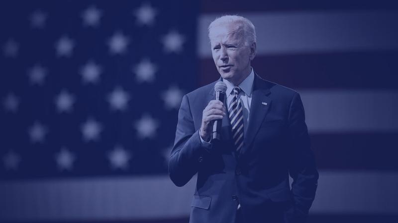 President Joe Biden holding microphone in front of the American flag.