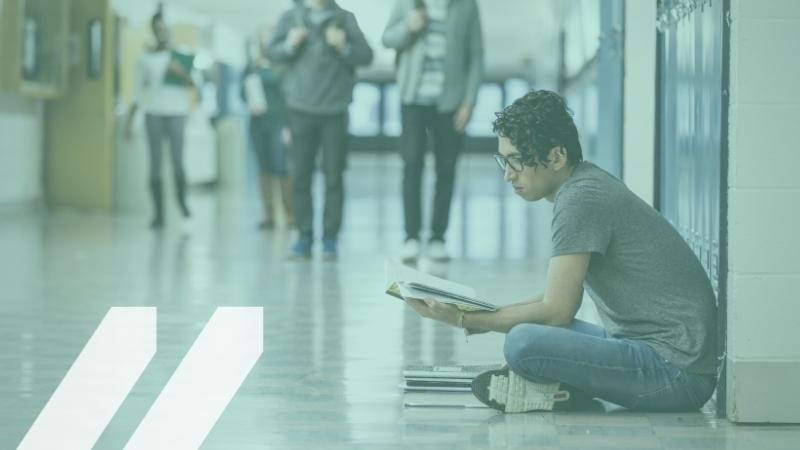 Image of a student sitting in a school hallway reading a book