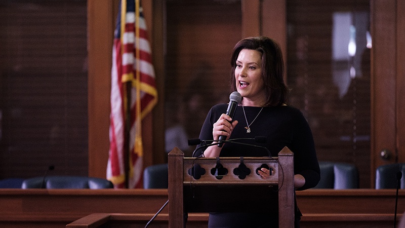 Governor Gretchen Whitmer holding microphone, speaking at podium